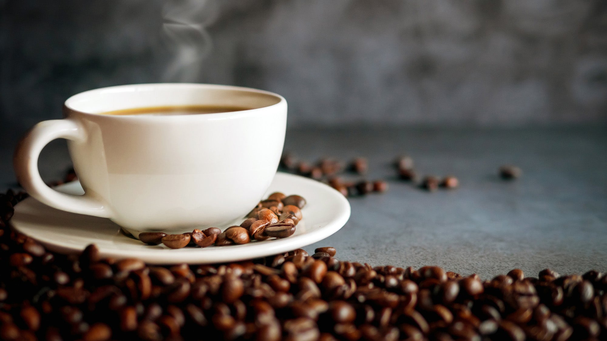 A steaming cup of coffee surrounded by coffee beans